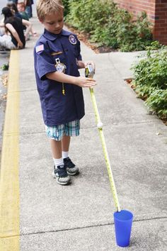 a young boy in uniform is holding a plastic cup and measuring the length of a pole