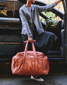 a woman sitting in the back of a car with her hand on an orange bag