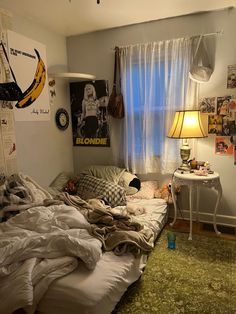 an unmade bed sitting in a bedroom next to a lamp and pictures on the wall