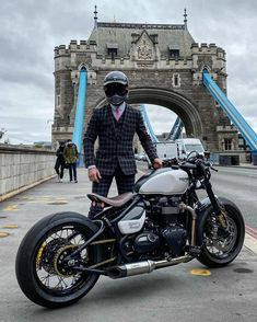 a man in a suit and tie standing next to a motorcycle on the street near a bridge