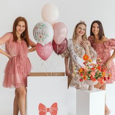 three beautiful women standing next to each other with balloons and flowers in front of them