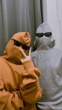 two people dressed in hoodies and sunglasses standing next to each other with their fingers up