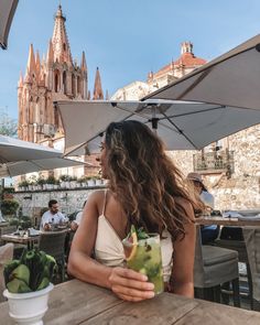 a woman sitting at an outdoor table holding a drink