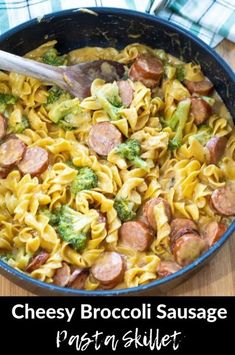 a skillet filled with pasta, sausage and broccoli on top of a wooden table