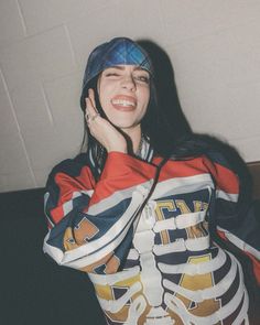 a young woman is smiling and holding her hand up to her face while wearing a hoodie