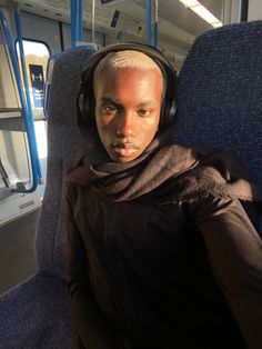 a man with headphones on sitting in a train looking at the camera while wearing ear muffs