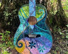 a colorful guitar sitting in the grass near a tree with leaves and swirls on it