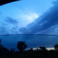 the sky is very dark and cloudy as seen through a car's rear view mirror