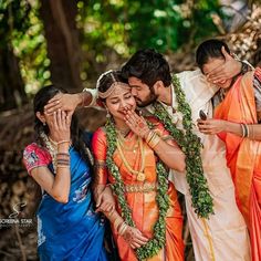 a group of people standing next to each other in front of trees and bushes with their faces covered by hands