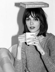 a woman sitting on a couch holding a coffee cup with a box on top of her head