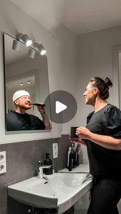 a woman brushing her teeth in front of a mirror with a man taking a selfie