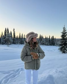 a woman standing in the snow with her hands on her hips wearing a hat and gloves