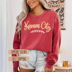 Show off your team spirit with our Women Kansas City Football Sweatshirt Apparel, designed for every KC football fan. This game day unisex pullover crewneck shirt is the perfect Kansas City sport fan clothing for staying comfortable and stylish. ✨𝐏𝐑𝐎𝐃𝐔𝐂𝐓 𝐃𝐄𝐓𝐀𝐈𝐋𝐒✨ ☆ Comfort Colors 1566 unisex sweatshirt ☆ 80% ring-spun cotton, 20% polyester ☆ 1x1 ribbed collar, cuffs, and bottom hem for stretch and a well-fitted garment ☆ Necktape: twill tape stabilizes the neck seam for comfort and Game Day Sweatshirt With Lettering In Relaxed Fit, Relaxed Fit Lettering Sweatshirt For Game Day, Collegiate Team-colored Top With Lettering, Collegiate Tops With Team-colored Lettering, Football Season Team Spirit Tops With Lettering, Football Season Crew Neck Top With Lettering, Sports Season Fan Apparel Sweatshirt With Lettering, Team Spirit Sweatshirt With Lettering For Fan Gear, Game Day Fan Apparel Top With Lettering