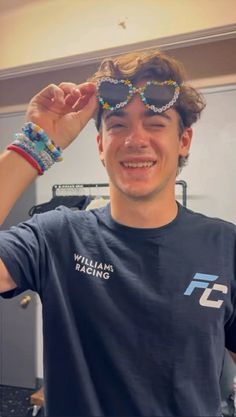 a man wearing sunglasses and beaded bracelets smiles at the camera while standing in front of a computer