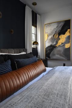 a bedroom with a large painting on the wall above the bed and leather headboard