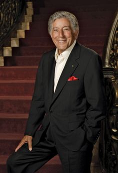 a man in a black suit and white shirt posing for a photo on some stairs