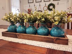 four blue vases with flowers in them on a wooden tray sitting on a table