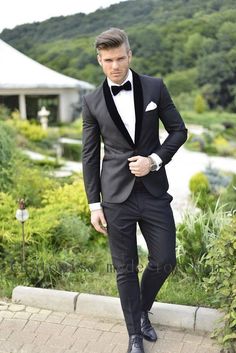 a man in a tuxedo and bow tie is standing on the sidewalk with his hands in his pockets