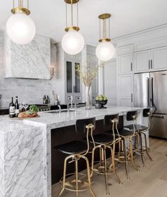 a kitchen with marble counter tops and gold stools in front of an island that has four lights hanging from the ceiling