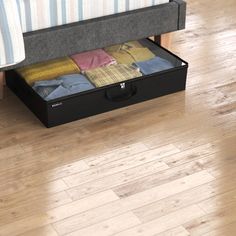 an open suitcase sitting on top of a wooden floor next to a bed with striped sheets