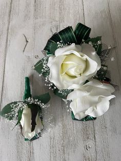 two white roses are sitting next to each other on a wooden surface with baby's breath