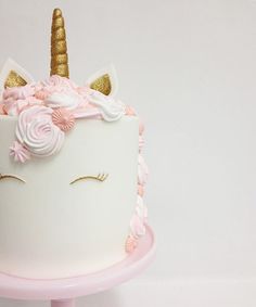 a white cake with pink icing and a gold horn on top that is decorated like a unicorn's head