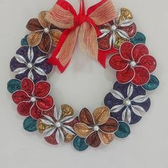 a christmas wreath made out of colored glass flowers with a red ribbon hanging on the wall