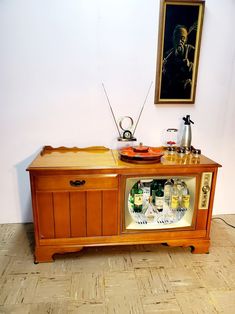 an old fashioned cabinet with drinks on it in front of a painting hanging on the wall