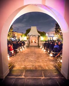 an outdoor ceremony with candles lit in front of the arch and people sitting on chairs