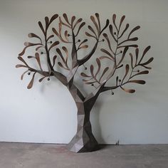 a metal tree sculpture sitting on top of a cement floor next to a white wall