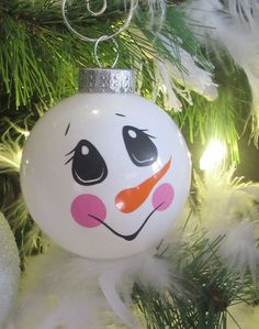 a white ornament with a snowman face on it hanging from a christmas tree