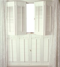 an open window with white shutters and curtains