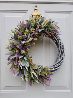 a wreath with purple flowers and greenery hangs on the front door's white paneled door