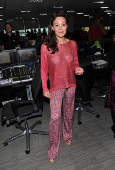 a woman standing in an office wearing pink and purple pajama pants, smiling at the camera