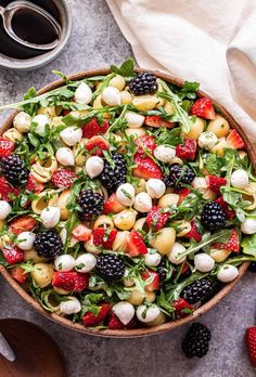 a salad with berries, spinach and mozzarella in a wooden bowl on a table