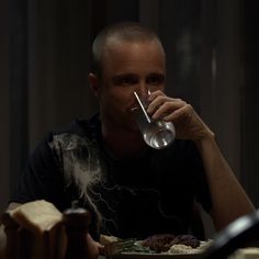 a man drinking from a wine glass while sitting at a table with food on it