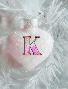 a pink ornament hanging from the side of a white christmas tree with letters k on it