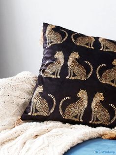 a black pillow with gold cheetah on it sitting on a bed next to a white blanket