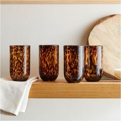 four glasses sitting on top of a wooden shelf next to a white towel and wood slice