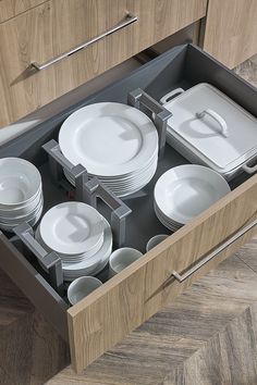 an open drawer in a kitchen filled with white plates and silverware on wooden flooring