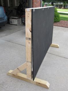 a large black screen sitting on top of a wooden stand in front of a garage