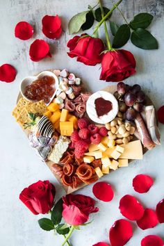 a heart shaped platter filled with cheese, fruit and nuts next to red roses