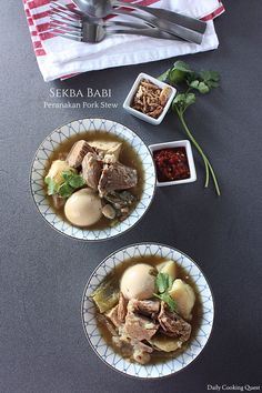 two bowls filled with meat and vegetables on top of a table next to utensils