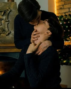 two people hugging each other in front of a fireplace