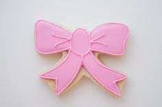 a cookie decorated with pink icing and a large bow on the top, sitting on a white surface