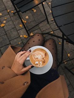 a woman sitting at an outdoor table with a cup of cappuccino in her hand