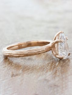 a close up of a ring with a diamond on the side and a twig in the middle