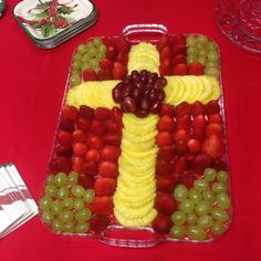 a cross made out of grapes and strawberries on a red table with other plates