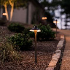 an outdoor lamp is lit up on the side of a sidewalk in front of some bushes