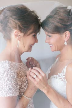 two women standing next to each other in front of a white wall wearing wedding dresses